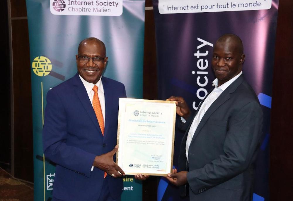 Two men in suits shake hands and hold a certificate