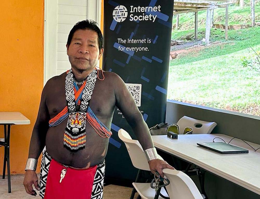A man stands in front of a charging computer and an Internet Society sign